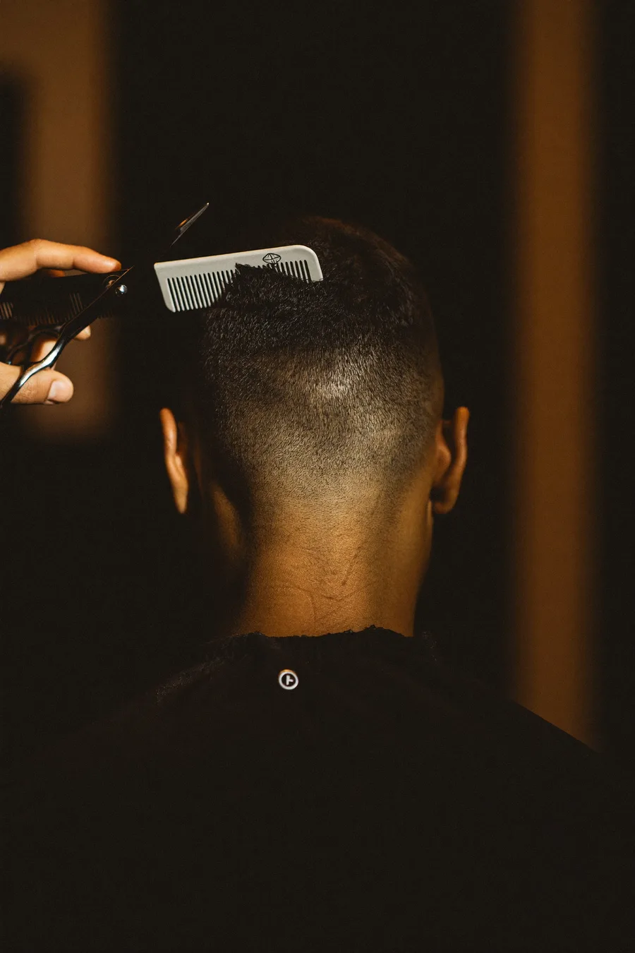 Schere und Kamm an einem sauberen Fade — Herrenhaarschnitt im warmen Barbershop-Licht