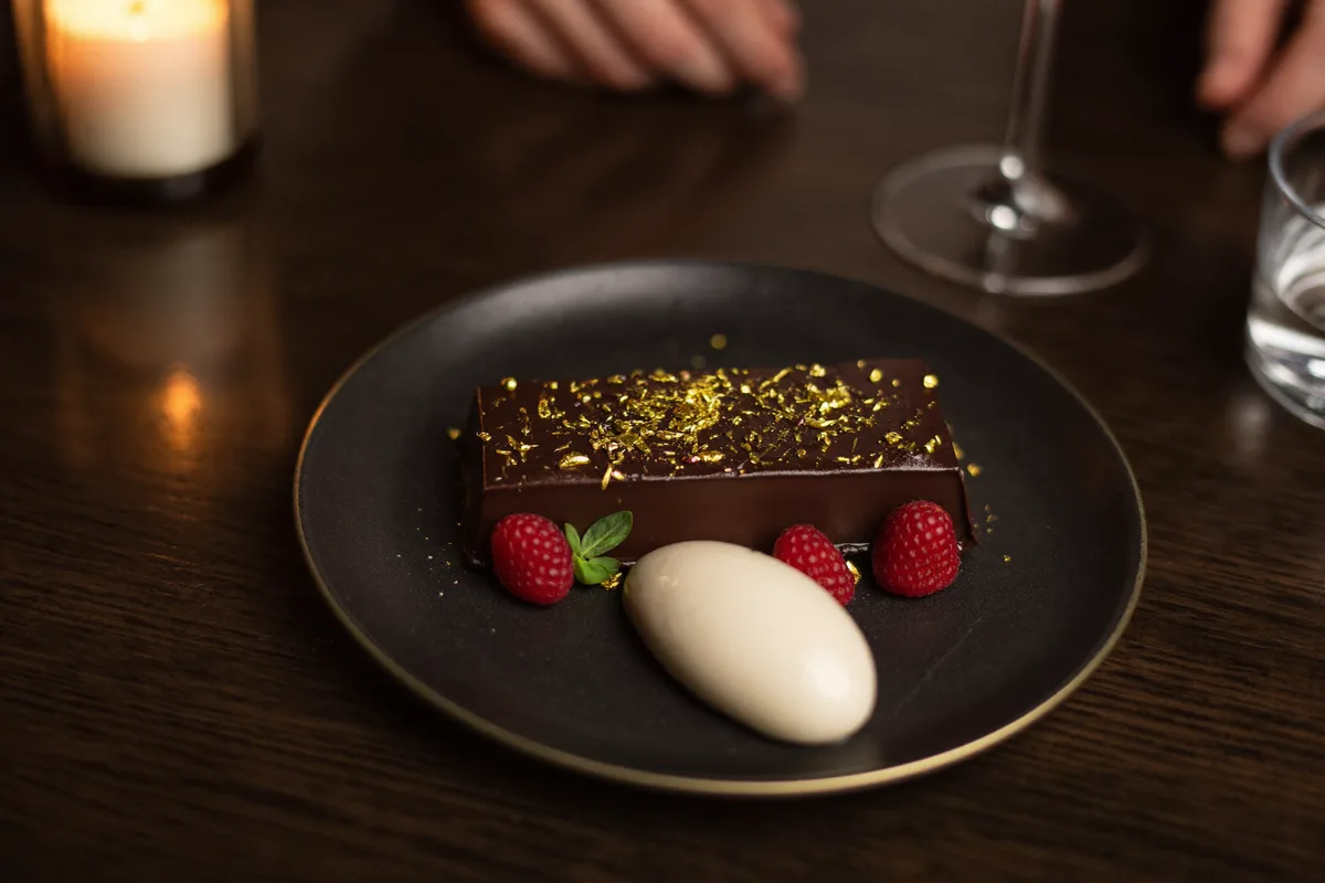 Elegant angerichtetes Dessert im warmen Kerzenlicht auf dunklem Holztisch