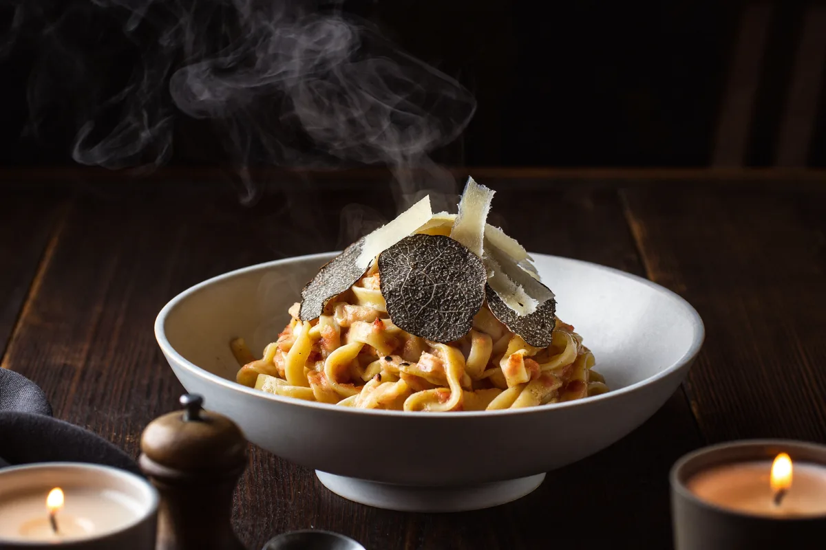 Frische Trüffel-Pasta mit Parmesanspänen und zartem Dampf auf dunklem Tisch