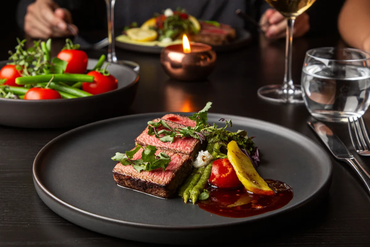 Aufgeschnittenes Signature Steak auf dunkler Keramik mit Jus im Kerzenlicht