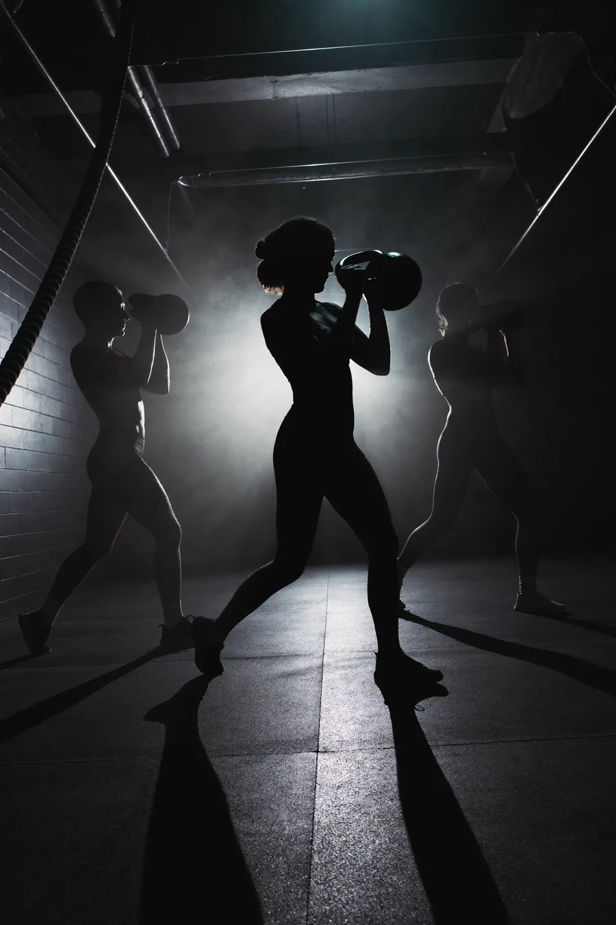 Kleine Trainingsgruppe als Silhouetten mitten im Workout im dunklen Premium-Gym