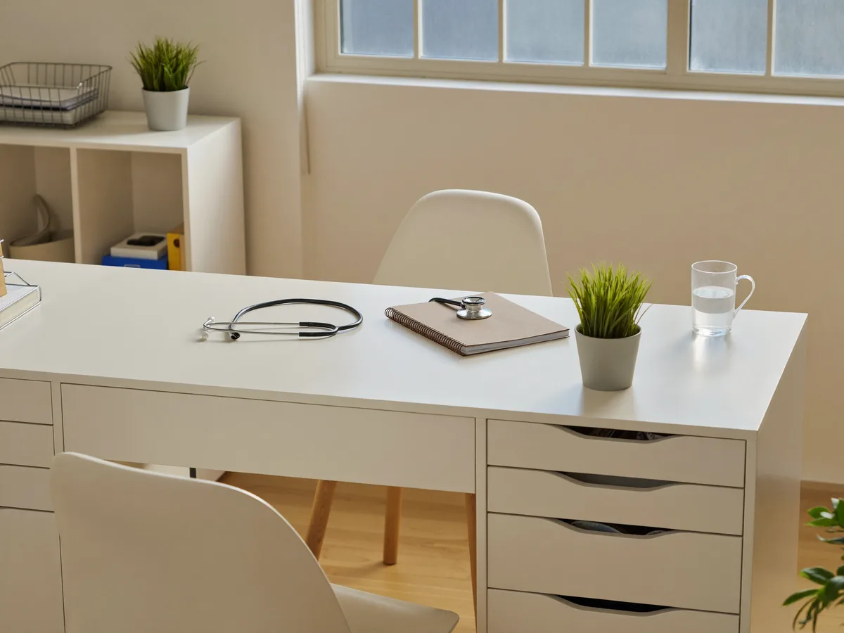 Heller Schreibtisch im Sprechzimmer mit Stethoskop und Notizbuch im Tageslicht